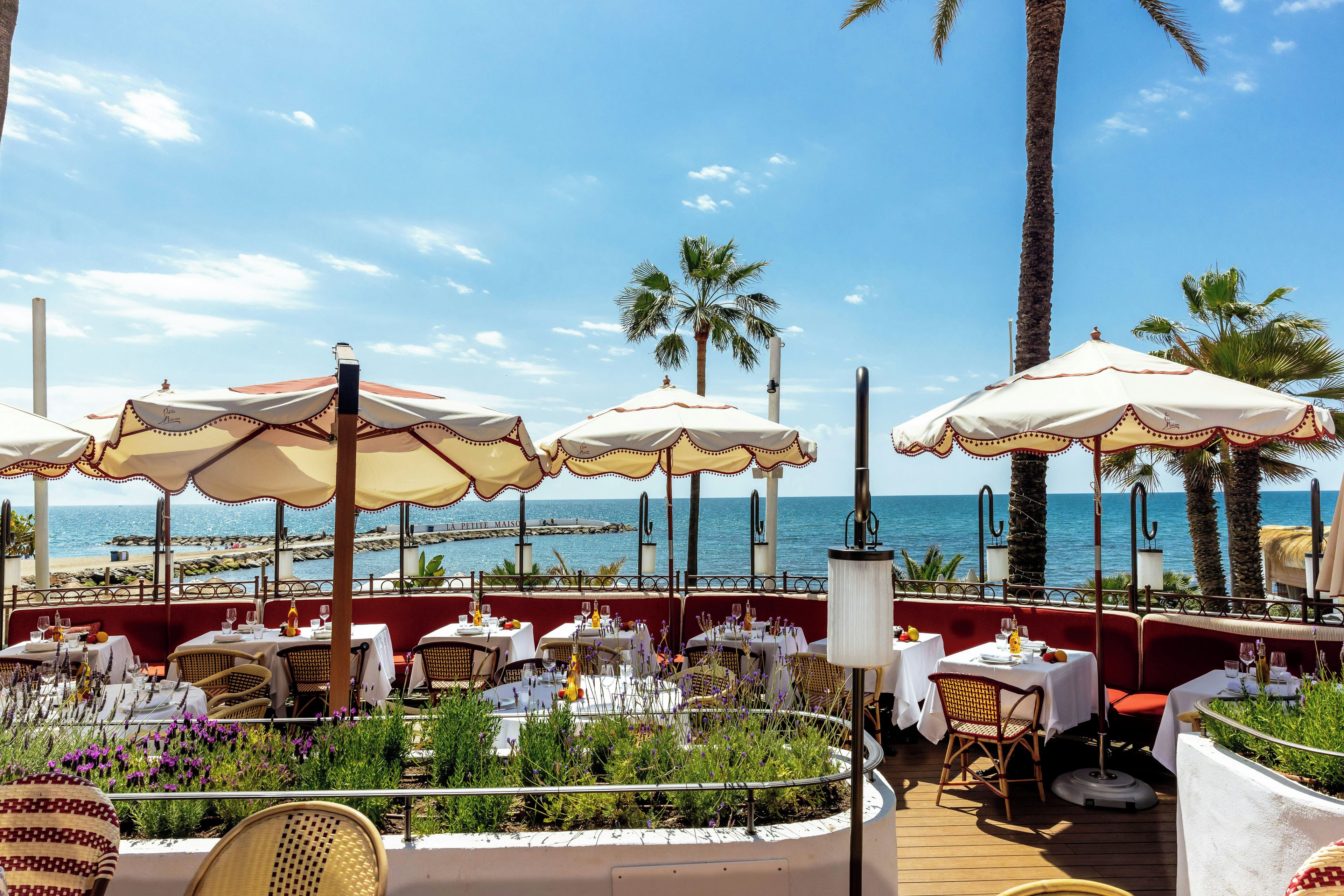 An outdoor dining area with tables and chairs, umbrellas, and a view of the sea.