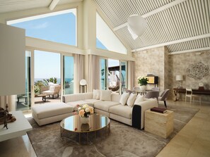 A spacious living room with a large sofa, a glass coffee table, and a view of the ocean. - Puente Romano Marbella (Marbella)