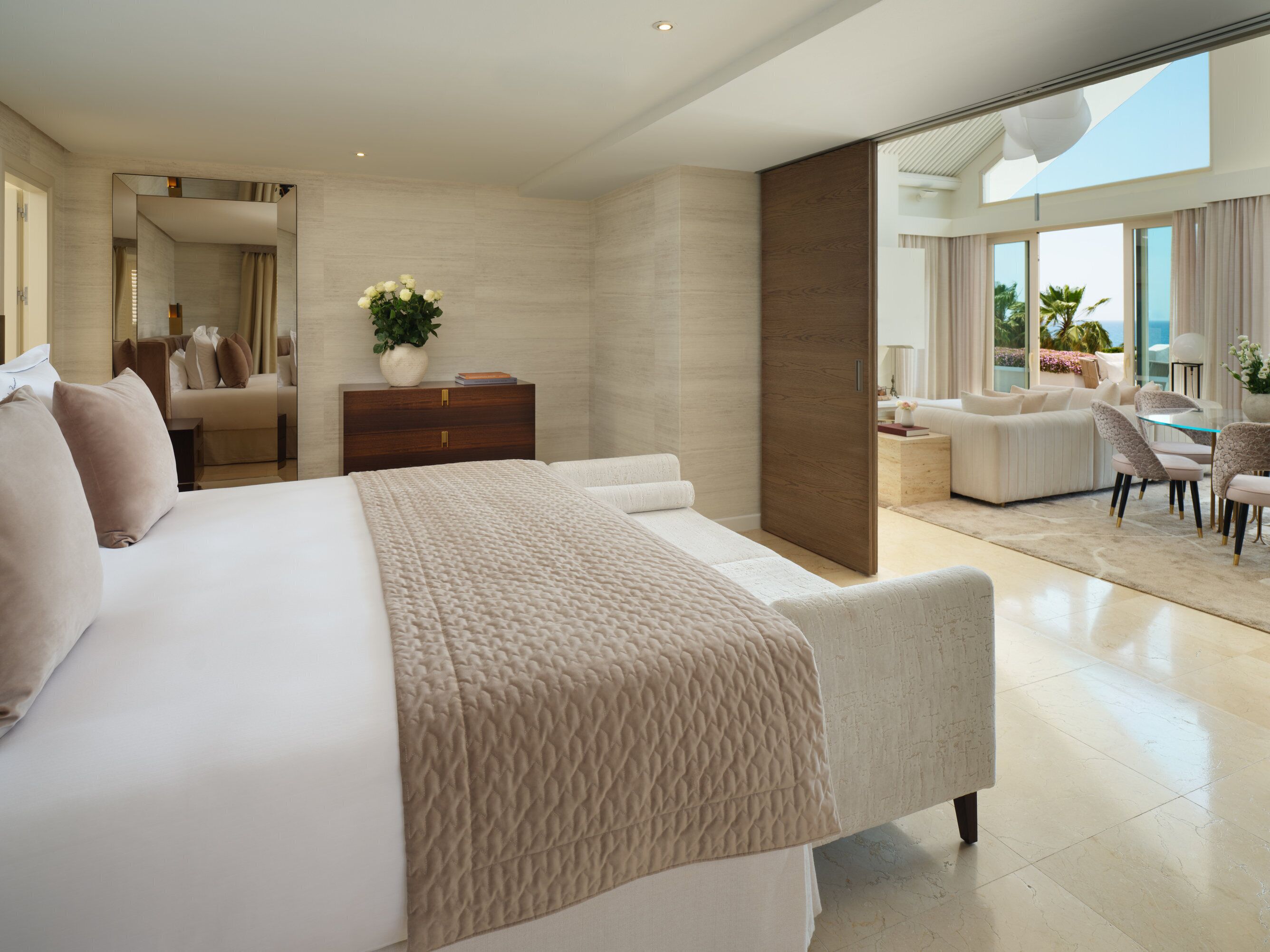 Een moderne slaapkamer met een groot bed, een houten nachtkastje, een potplant en uitzicht op de oceaan door grote ramen.