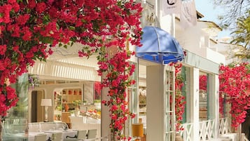A restaurant with outdoor seating, white tables, and a blue umbrella.