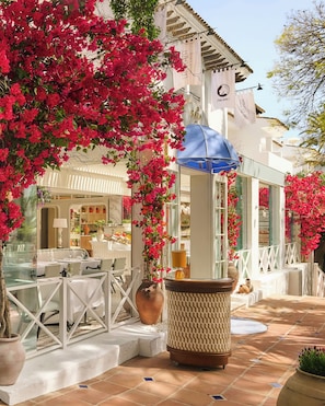 A restaurant with outdoor seating, white tables, and a blue umbrella. - Puente Romano Marbella (Marbella)