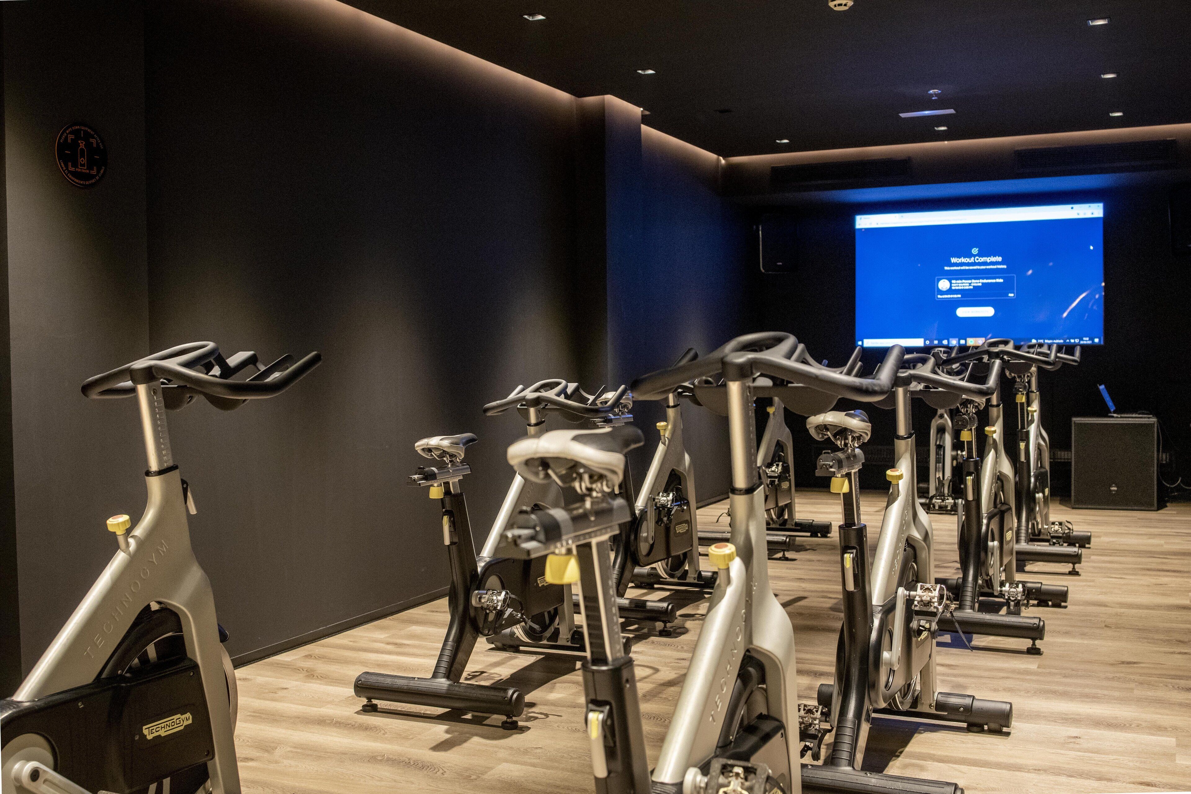 Varias bicicletas estáticas en un gimnasio, con una pantalla grande mostrando un mensaje de finalización de entrenamiento.