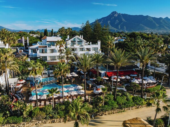 A resort with multiple buildings, a swimming pool, and palm trees. - Puente Romano Marbella (Marbella)
