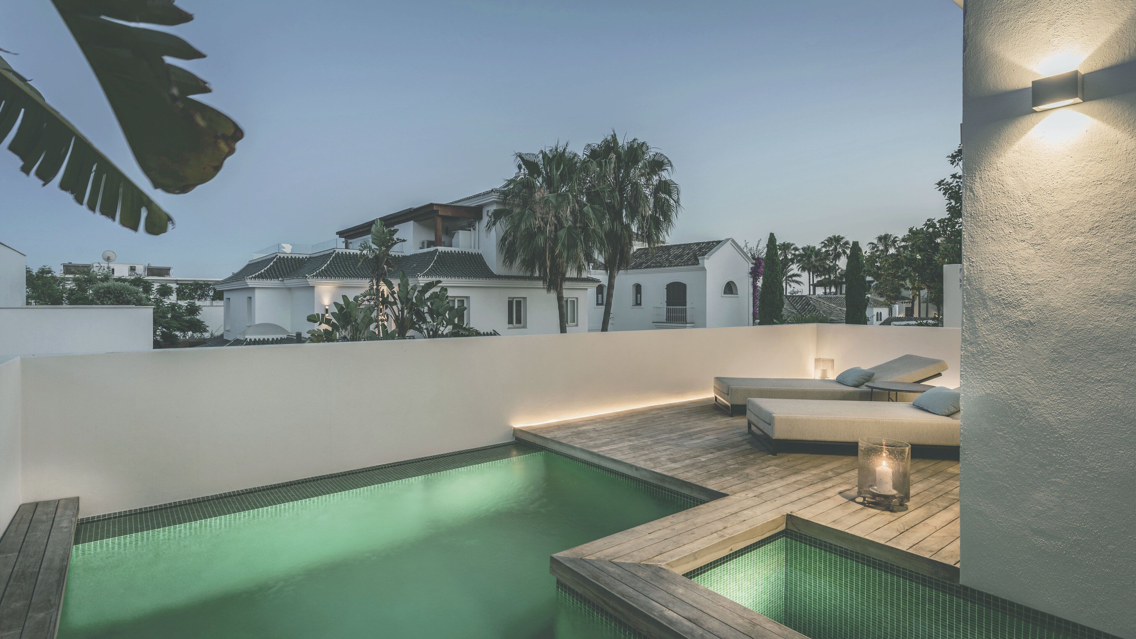 Zona de piscina en la azotea con terraza de madera, sillas de descanso y vistas a edificios tradicionales al fondo.