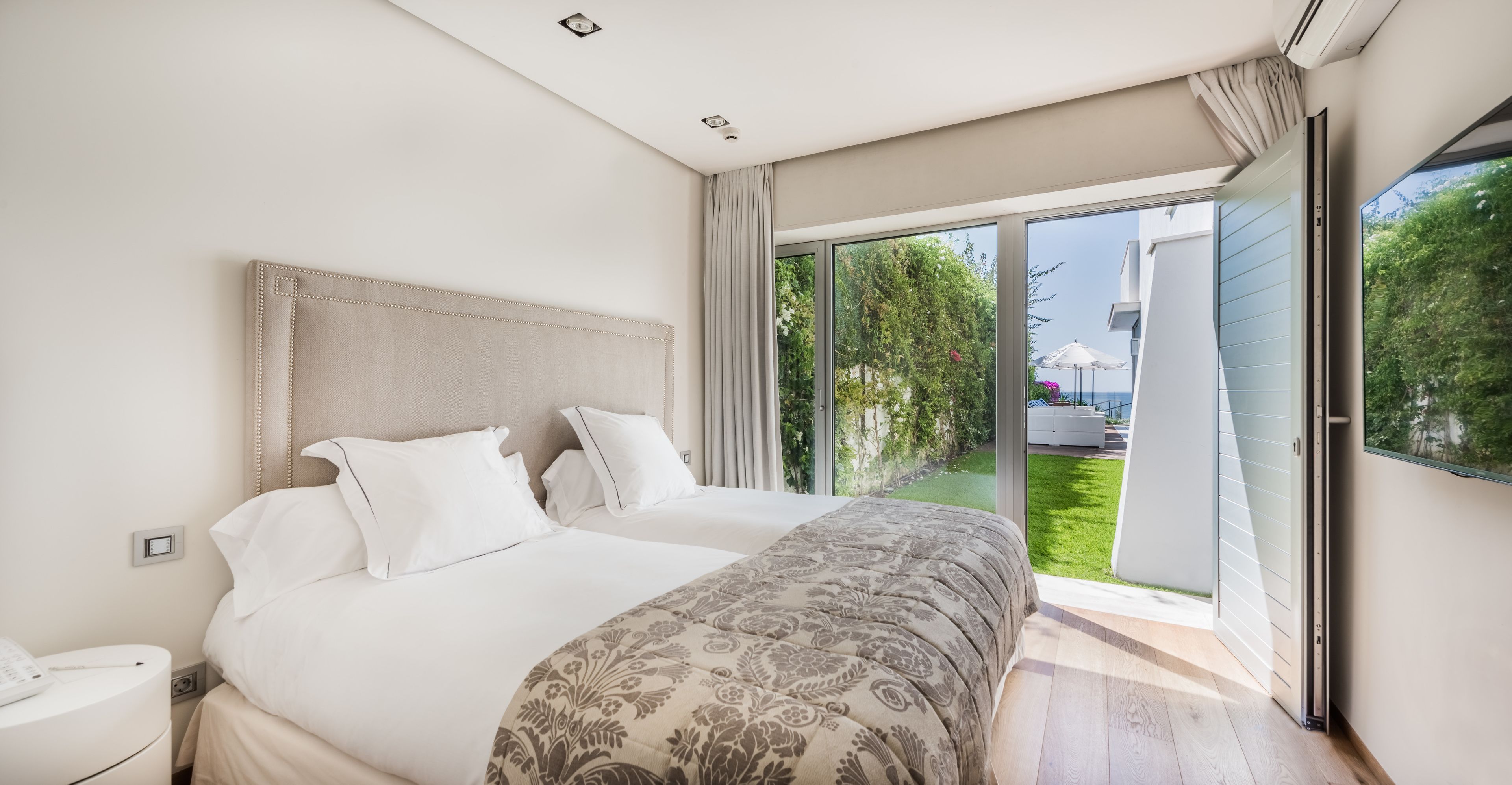 Een moderne slaapkamer met een groot bed, een nachtkastje en een schuifdeur naar een balkon.