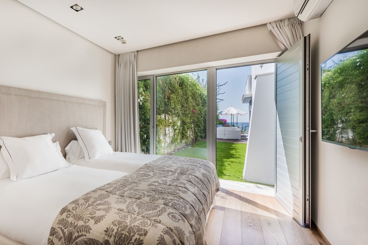A modern bedroom with a large bed, a nightstand, and a sliding glass door leading to a balcony.