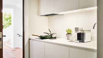 A modern kitchen with white cabinets, a stove, a coffee maker, and a potted plant.