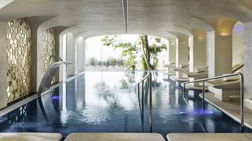 An indoor infinity pool with a view of trees, surrounded by white walls and seating areas.