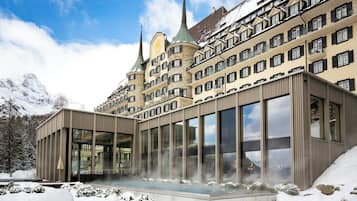 A modern hotel with a glass facade, a traditional building with spires in the background, and snow-covered surroundings.