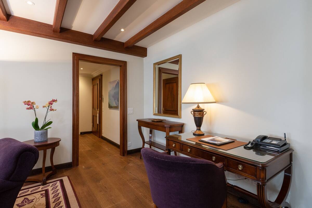 A hotel room with a wooden desk, a lamp, a telephone, and a purple chair.