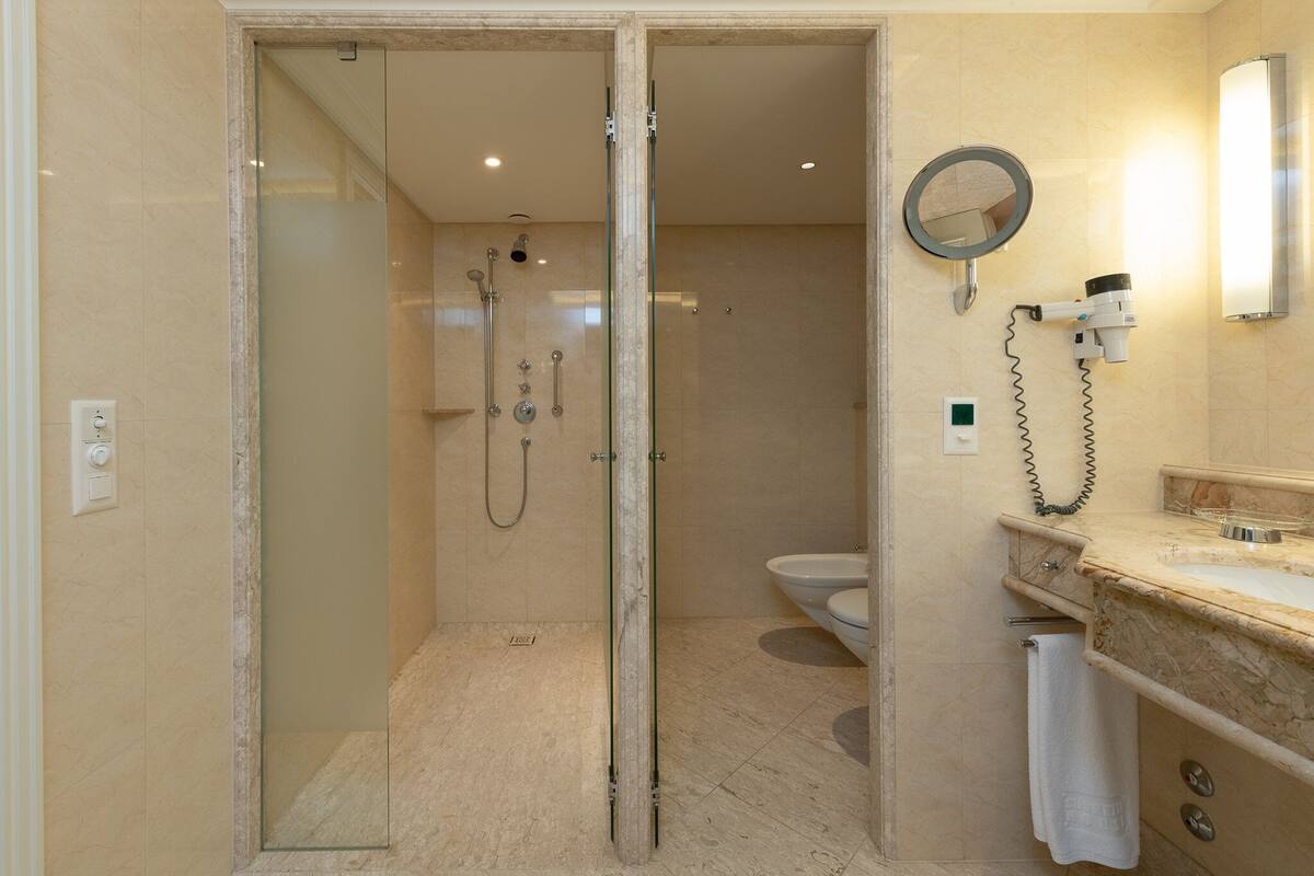 A modern bathroom with a glass-enclosed shower, a vanity with a marble countertop, and a toilet.