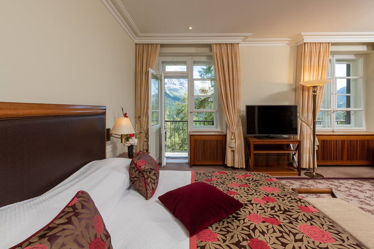 A hotel room with a bed, a TV, and a view of mountains through the window.