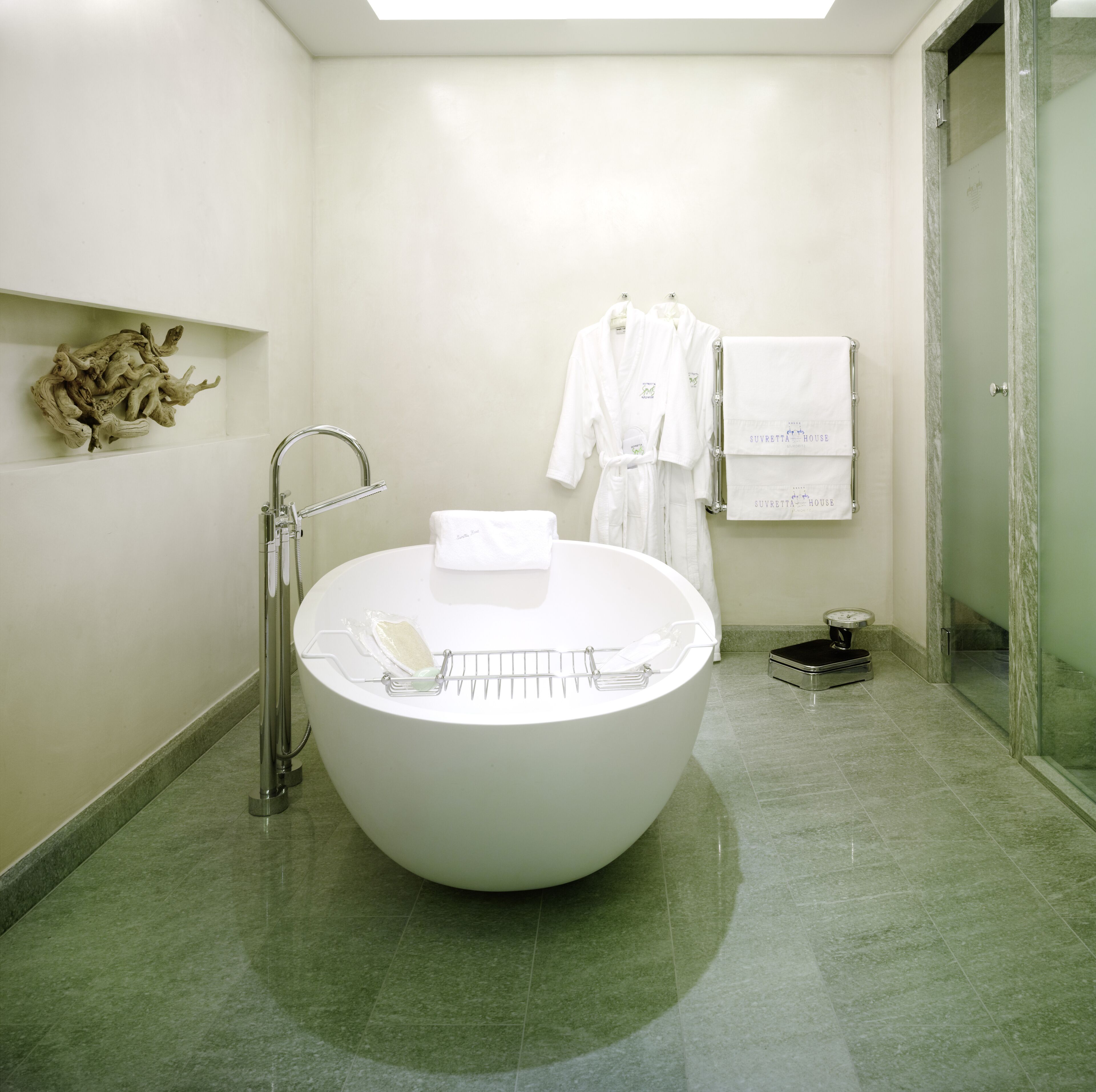 Un baño moderno con una bañera independiente grande, un perchero con batas y una balanza en el suelo.