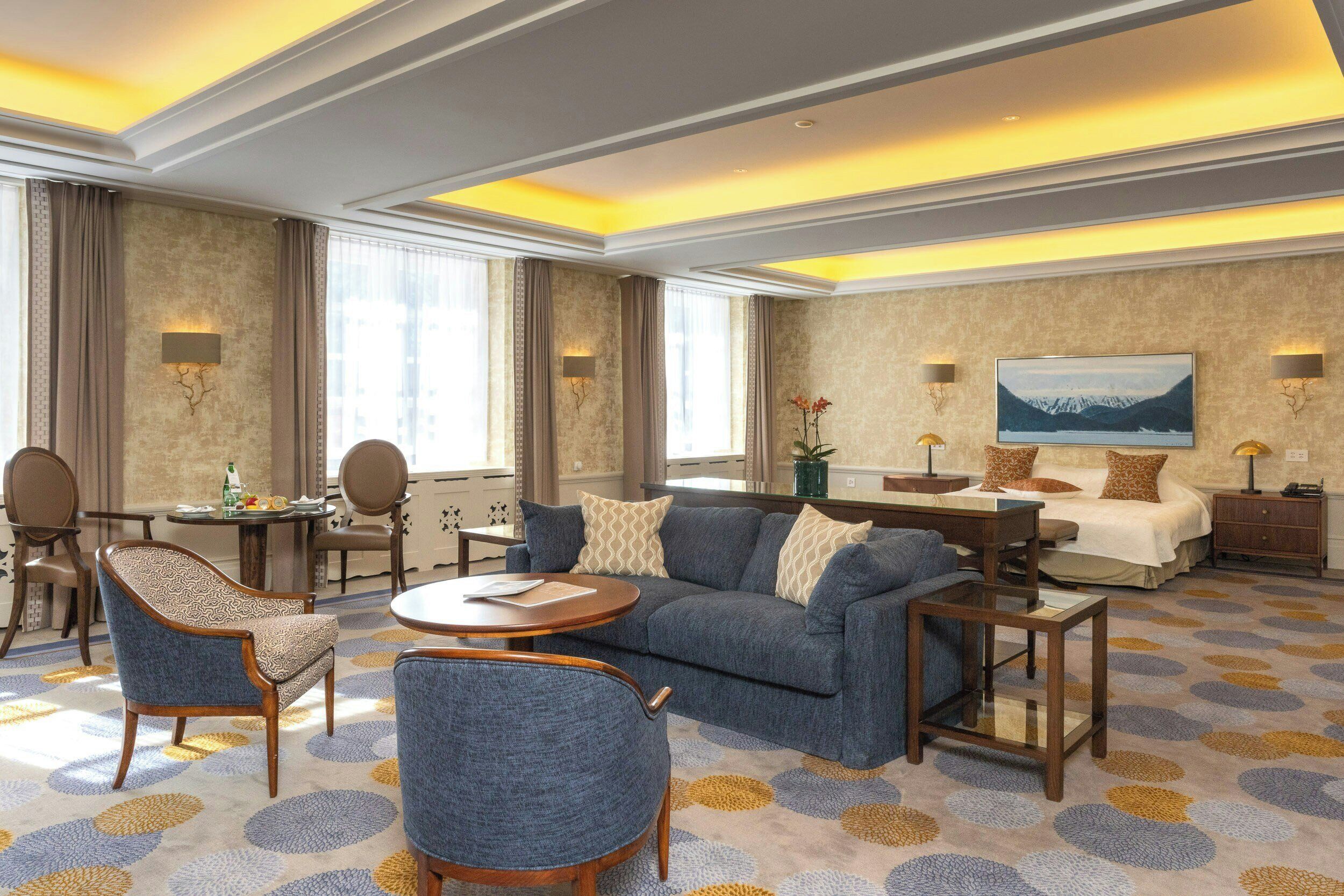 Ein Hotelzimmer mit einer Couch, Sesseln, einem kleinen Tisch, einem Bett und einem Fernseher.