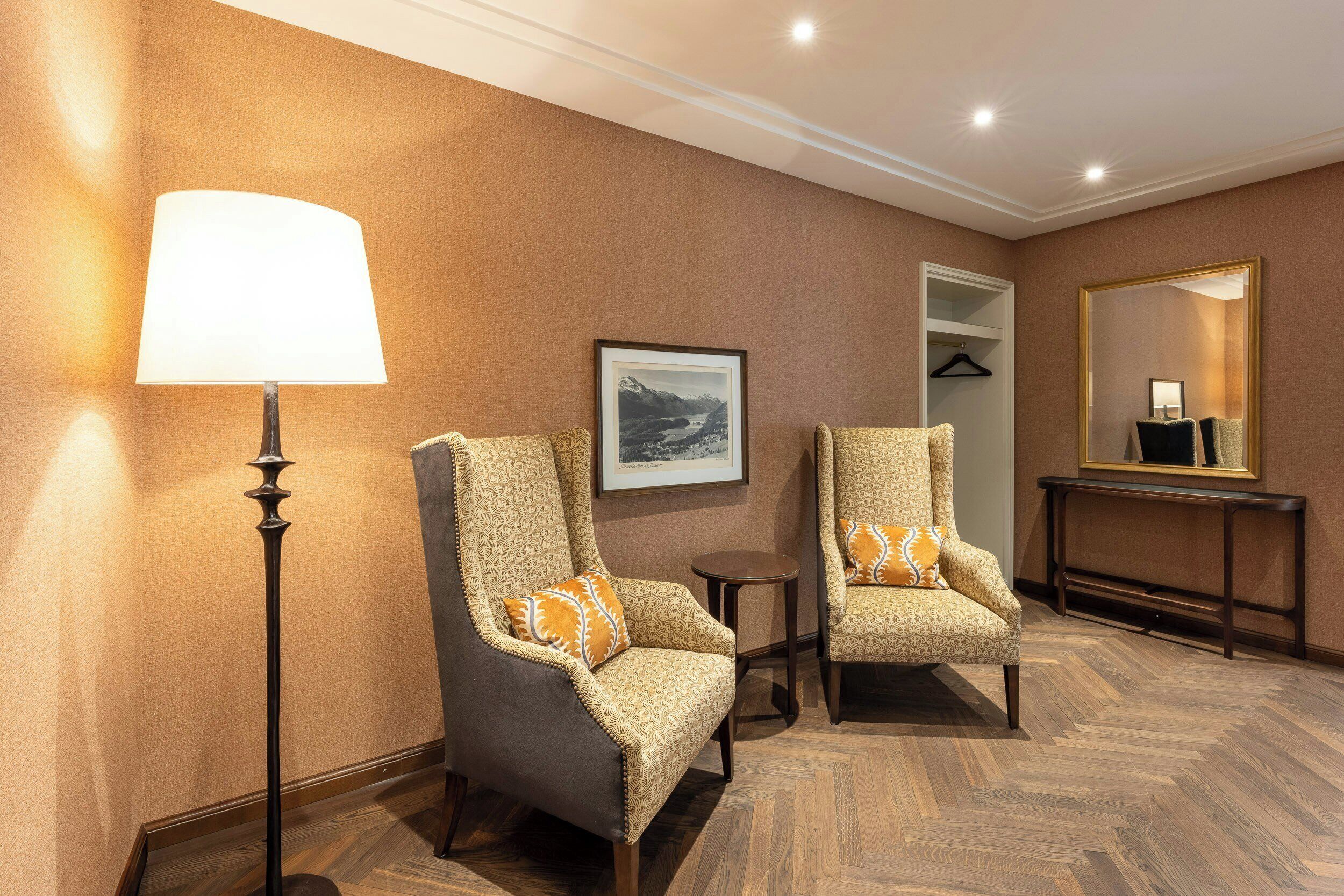 Une chambre d’hôtel avec deux fauteuils, une lampe sur pied, un tableau encadré au mur, un miroir et une console.