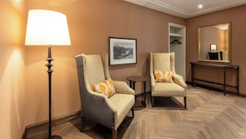 Une chambre d’hôtel avec deux fauteuils, une lampe sur pied, un tableau encadré au mur, un miroir et une console.