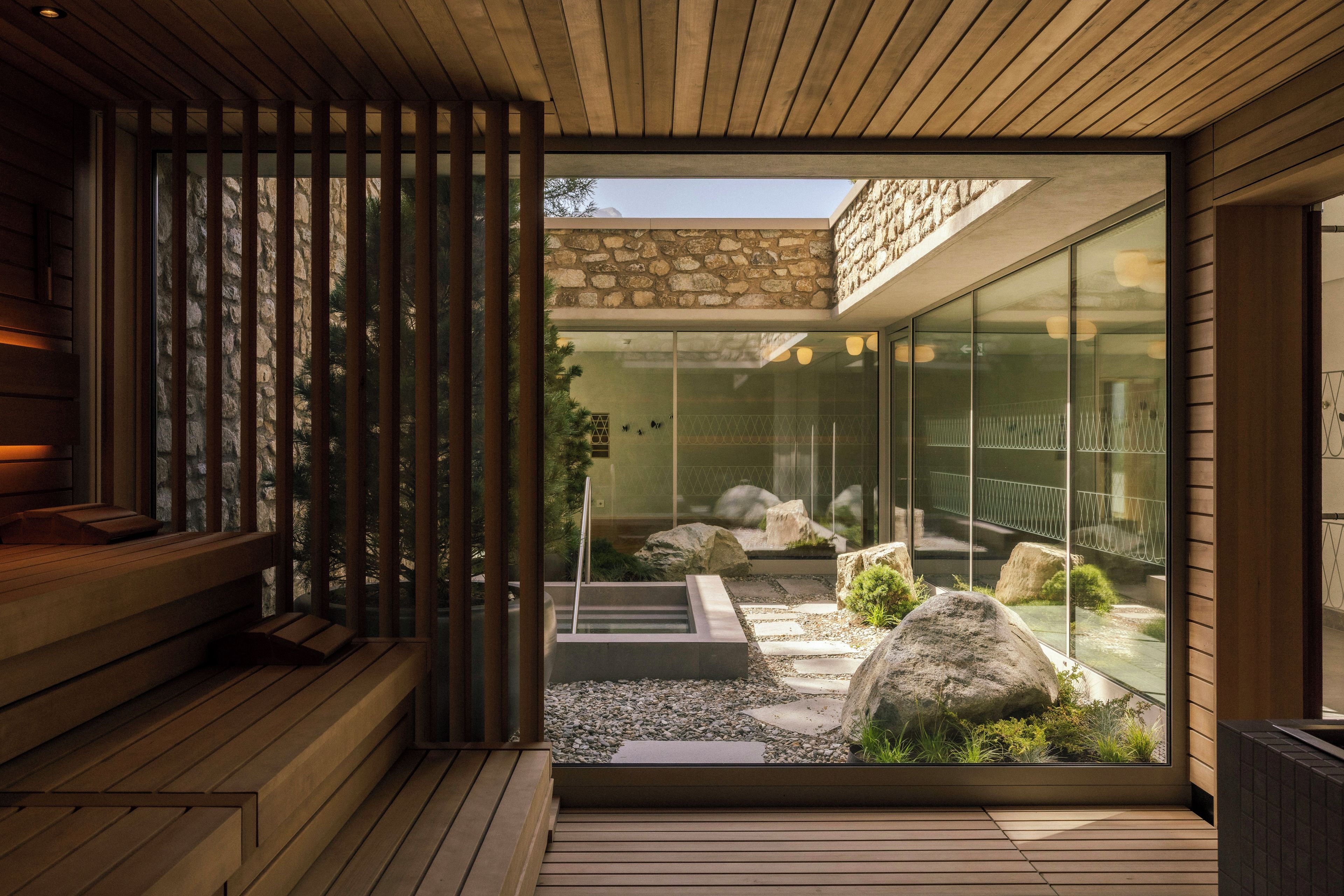 A modern interior with a wooden bench, a glass door leading to a garden with rocks and plants.
