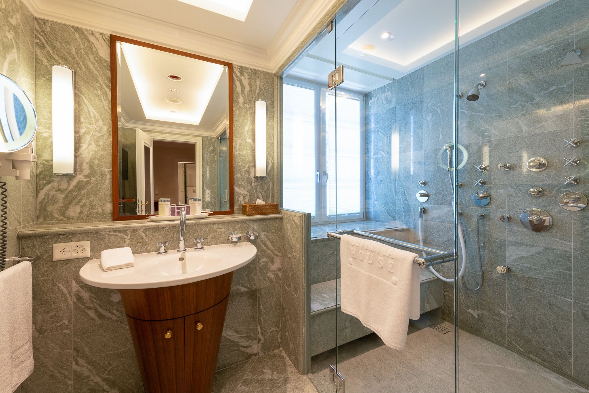 Une salle de bain moderne avec un meuble-lavabo en marbre, un grand miroir, une douche à parois de verre et un porte-serviettes.