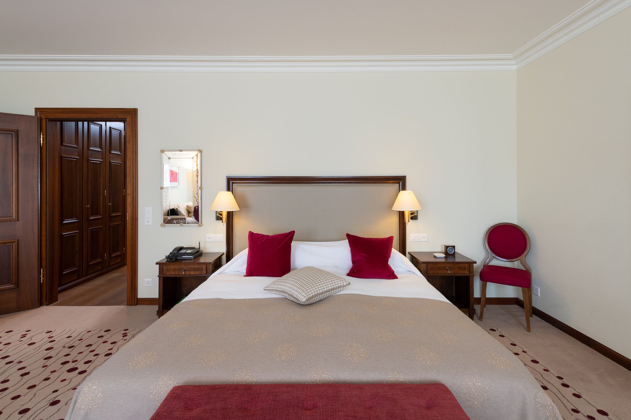 A hotel room with a large bed, two bedside tables, a chair, a mirror, and a wardrobe.