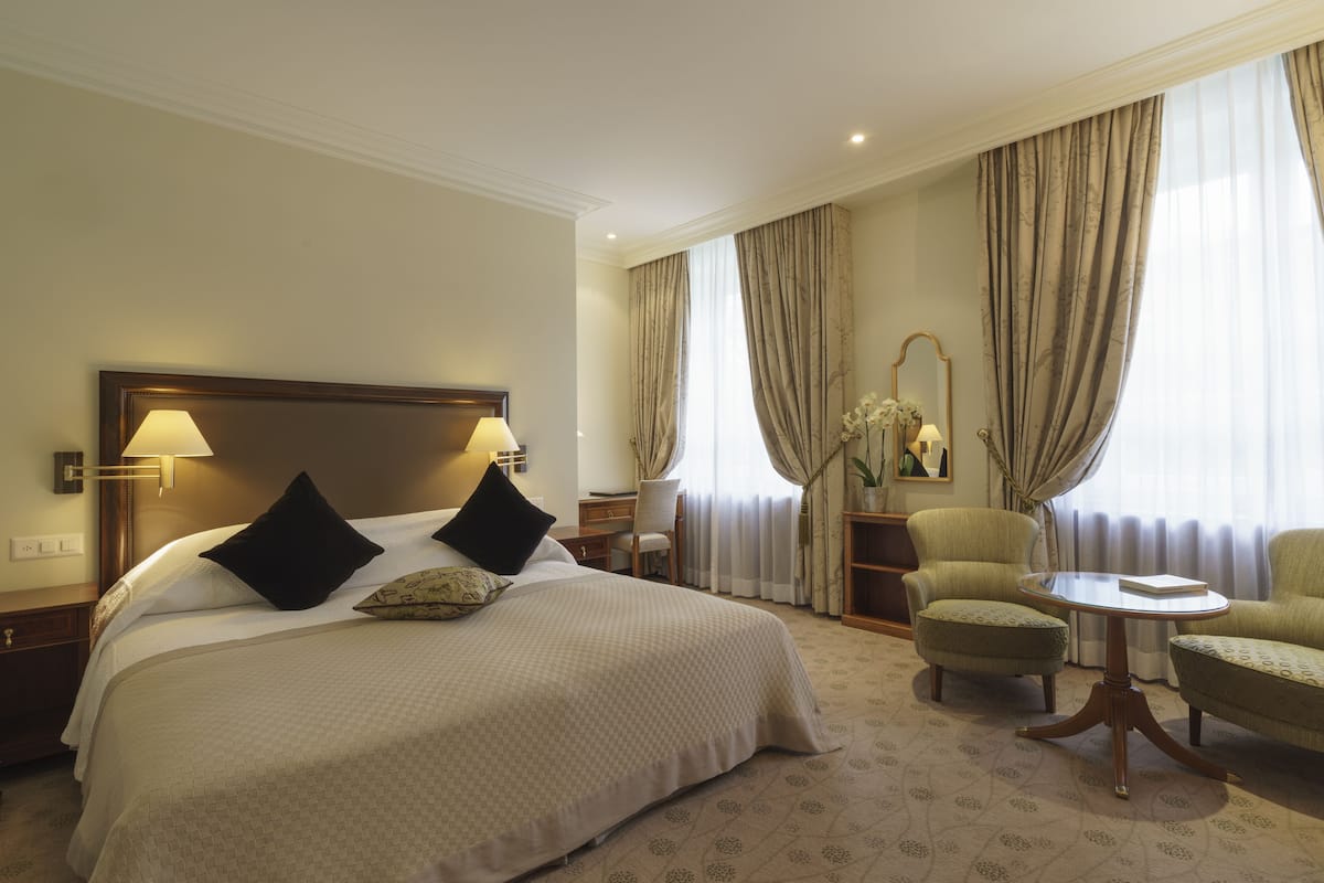 A hotel room with a large bed, two chairs, a small table, and a desk.