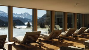 Ein Zimmer mit großen Fenstern und Blick auf die Berge, Holzboden und mehrere Loungesessel.