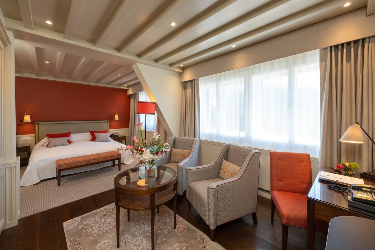 A hotel room with a bed, a sitting area with chairs, a coffee table, and a desk with a lamp.