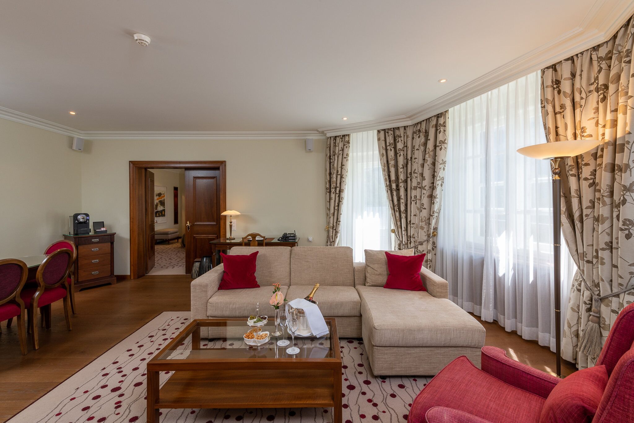 A living room with a sofa, red chairs, a coffee table, and a dining area with a table and chairs.