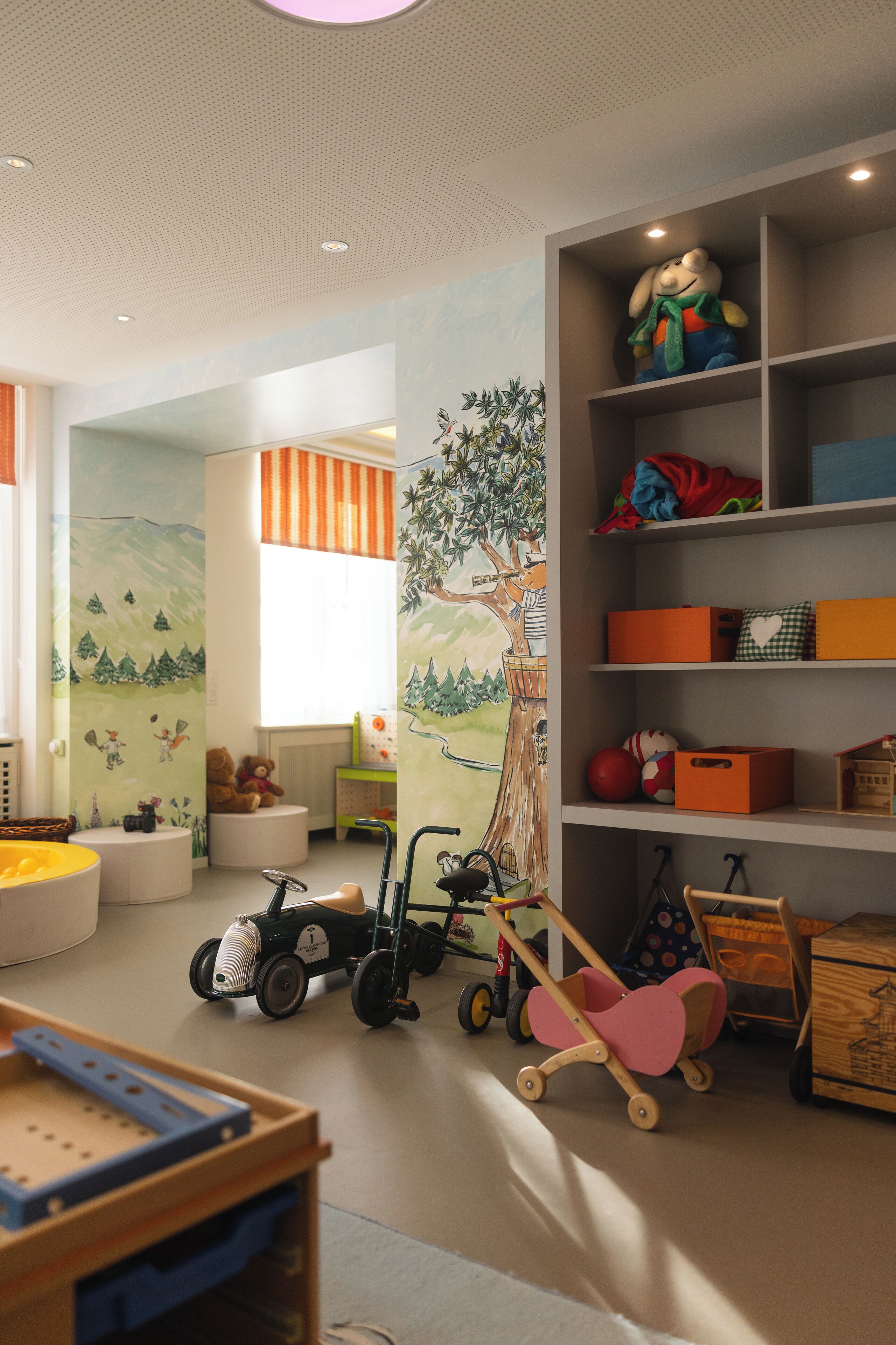 Un cuarto de juegos infantil con un mural grande, estantes con juguetes y un coche de juguete.
