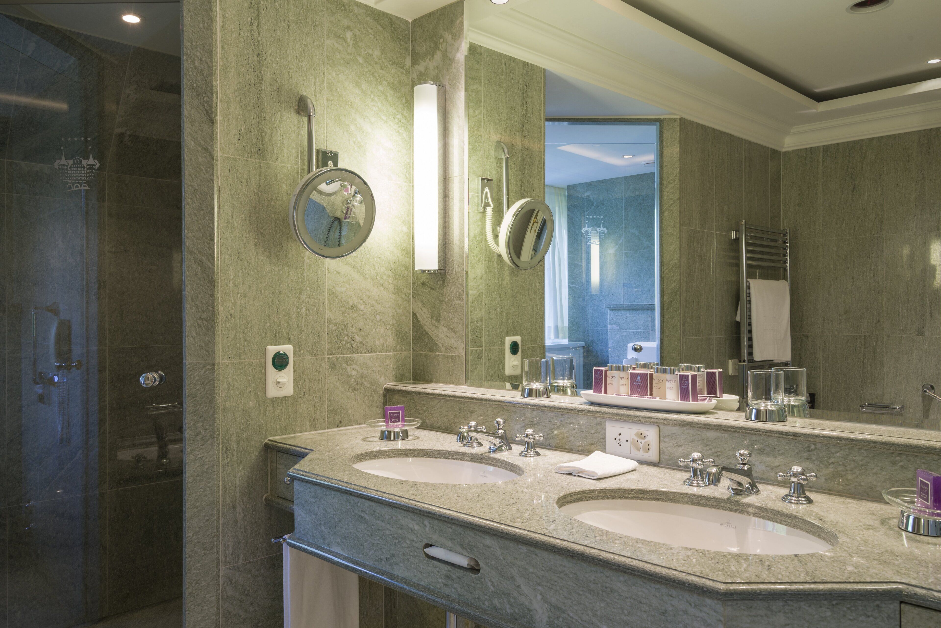 A modern bathroom with two sinks, a large mirror, and a glass shower enclosure.