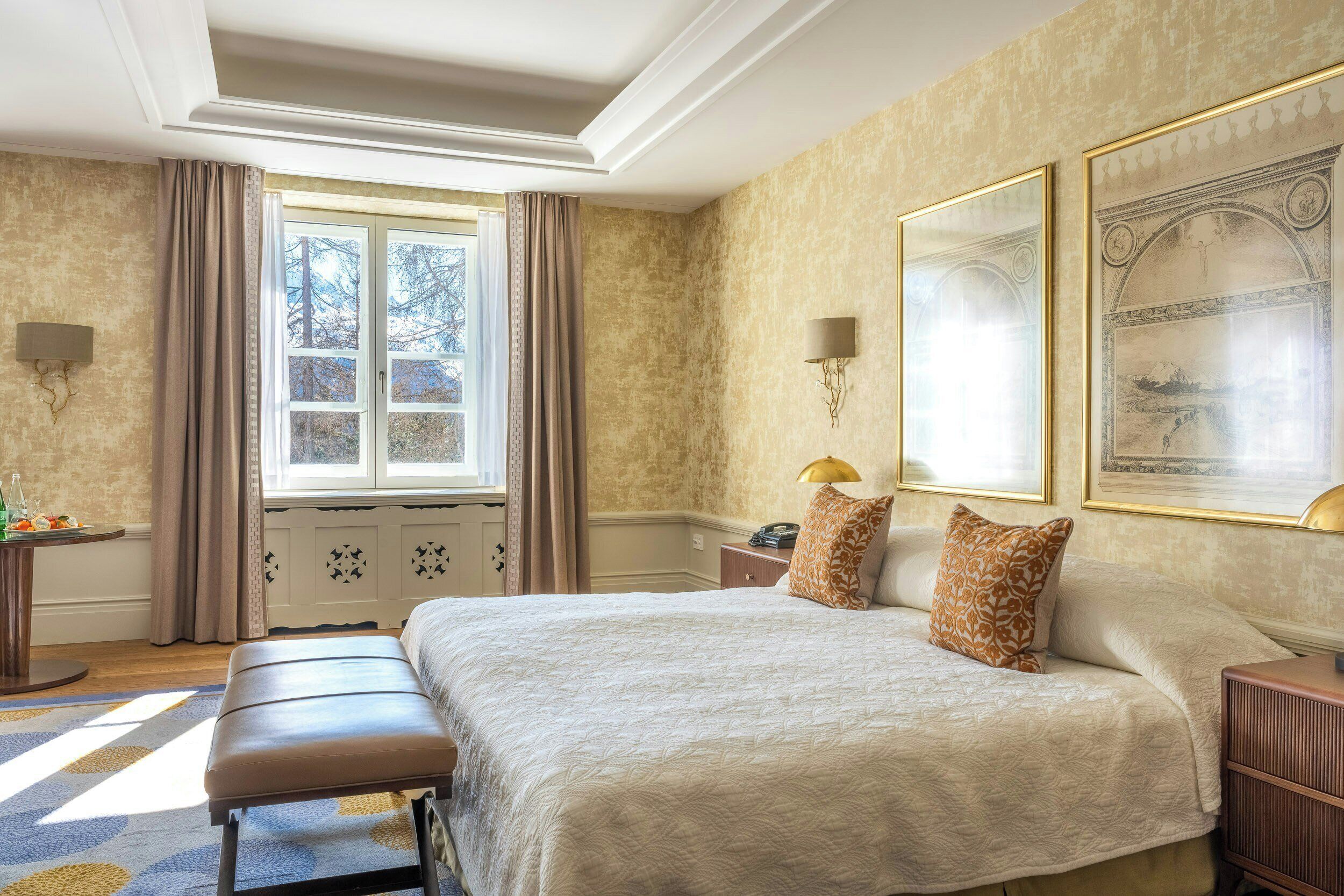 A well-appointed bedroom with a large bed, a bench, a nightstand, and a window with curtains.