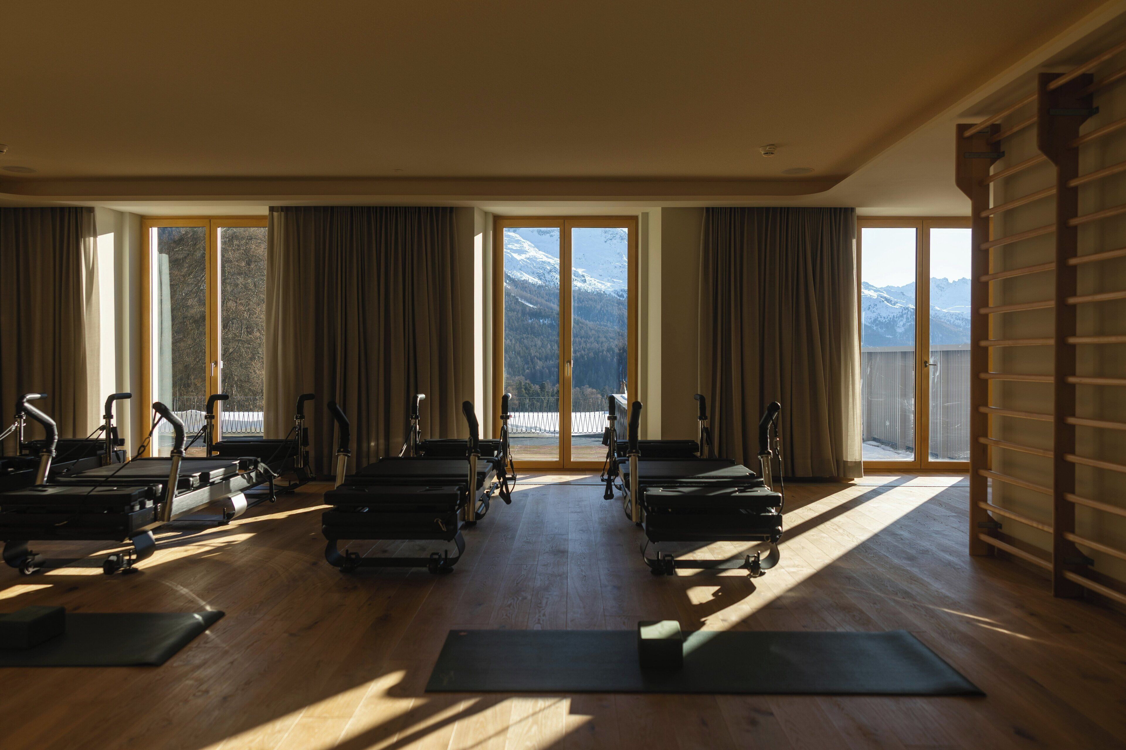 Ein geräumiger Fitnessraum mit Trainingsgeräten und großen Fenstern, welche Blick auf die Berge bieten.
