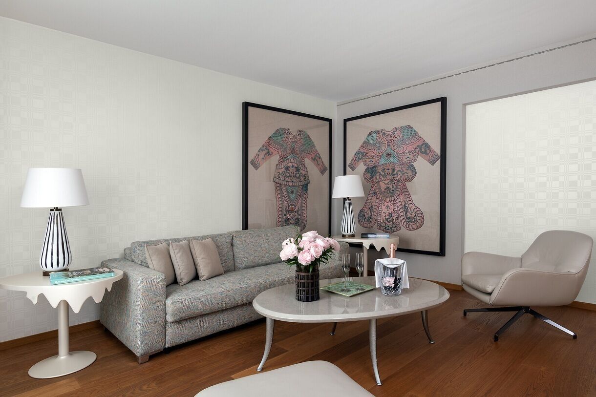 A modern living room with a grey sofa, a round coffee table with a vase of flowers, a white side table with a lamp, and a beige armchair.