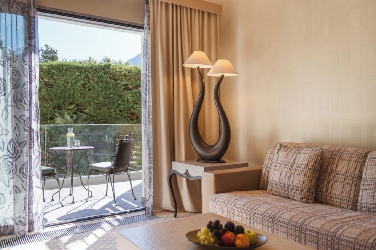 A hotel room with a balcony, a sofa, a table with fruit, and two floor lamps.
