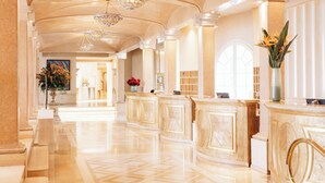 A spacious lobby with marble floors, elegant chandeliers, and a reception desk with a vase of flowers. - Hotel Eden Roc (Ascona)