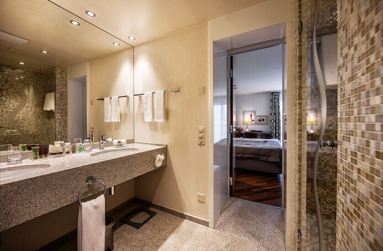 Ein modernes Badezimmer mit einer Granit-Arbeitsplatte, zwei Waschbecken, einem großen Spiegel und einer Duschkabine aus Glas.