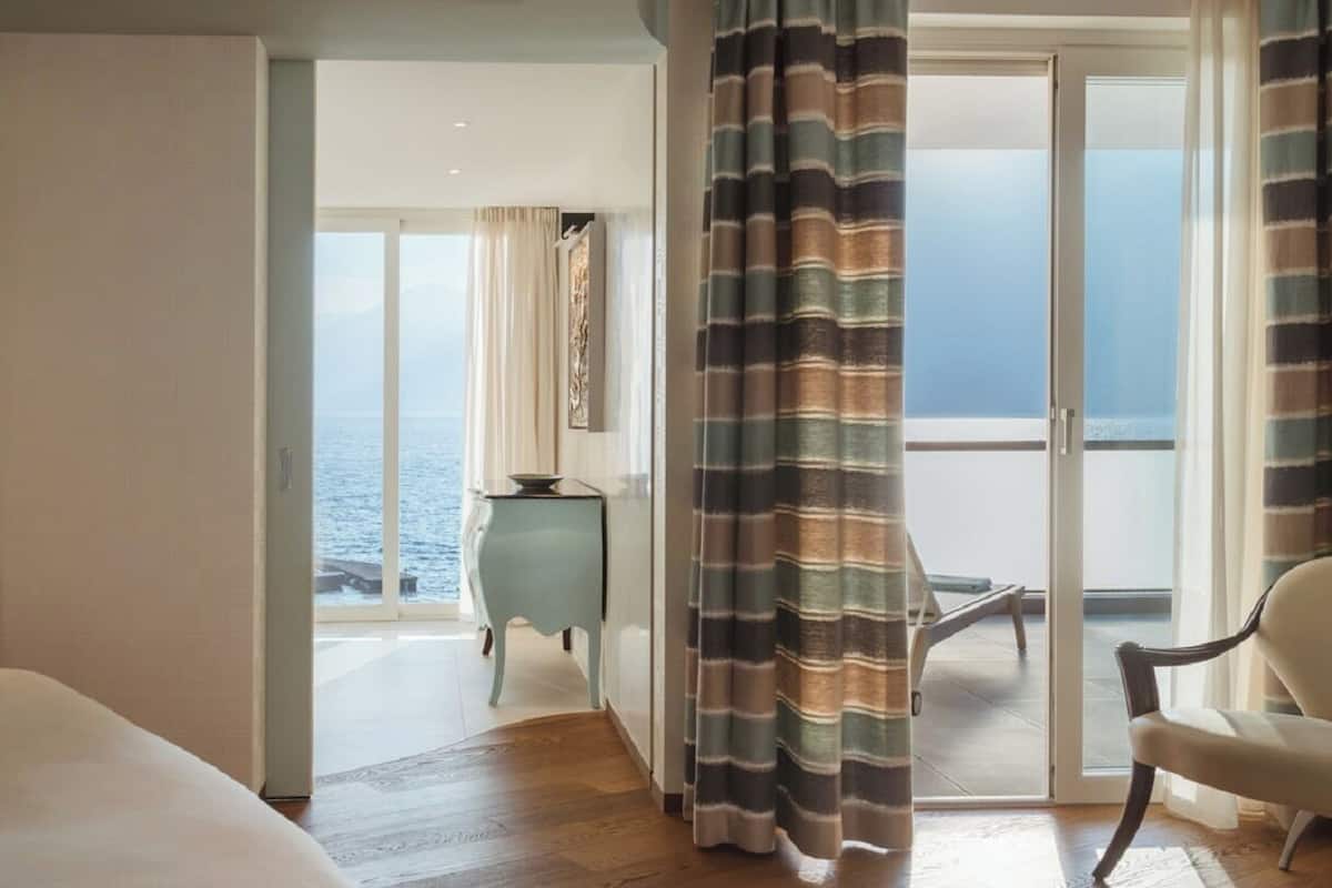 A hotel room with a view of the sea, a sliding glass door, a small side table, and a chair.