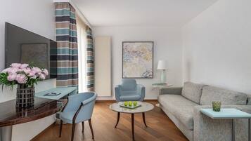 A modern living room with a sofa, a blue armchair, a round coffee table, and a desk with a vase of flowers.
