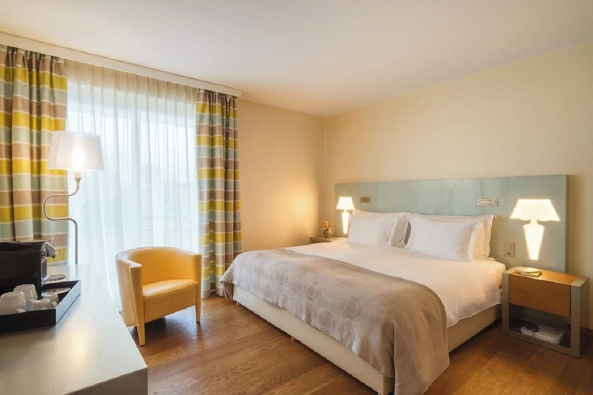 A hotel room with a bed, bedside tables, a chair, and a desk with a lamp.