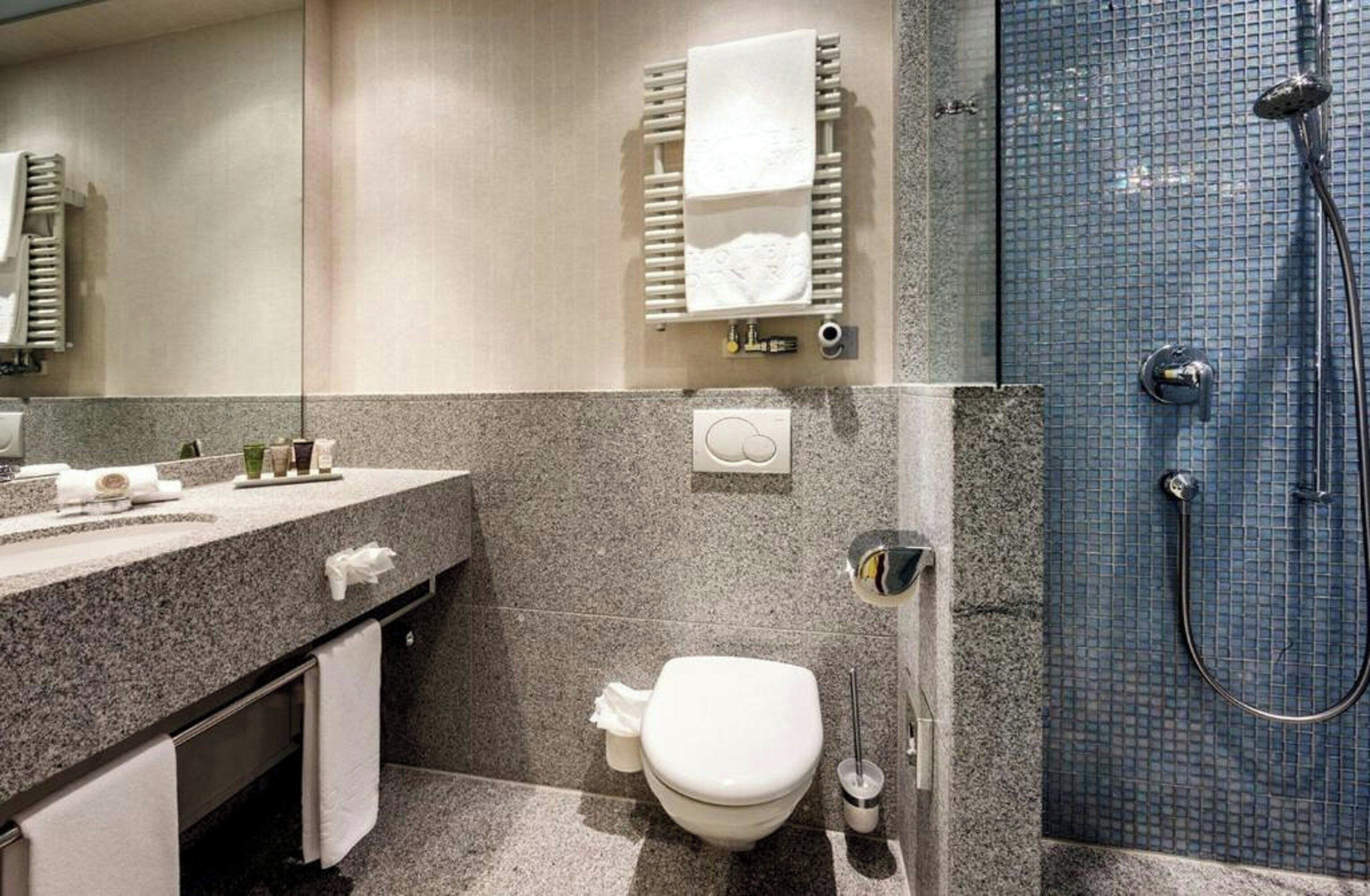 Un baño moderno con encimera de granito, inodoro, toallero y zona de ducha.