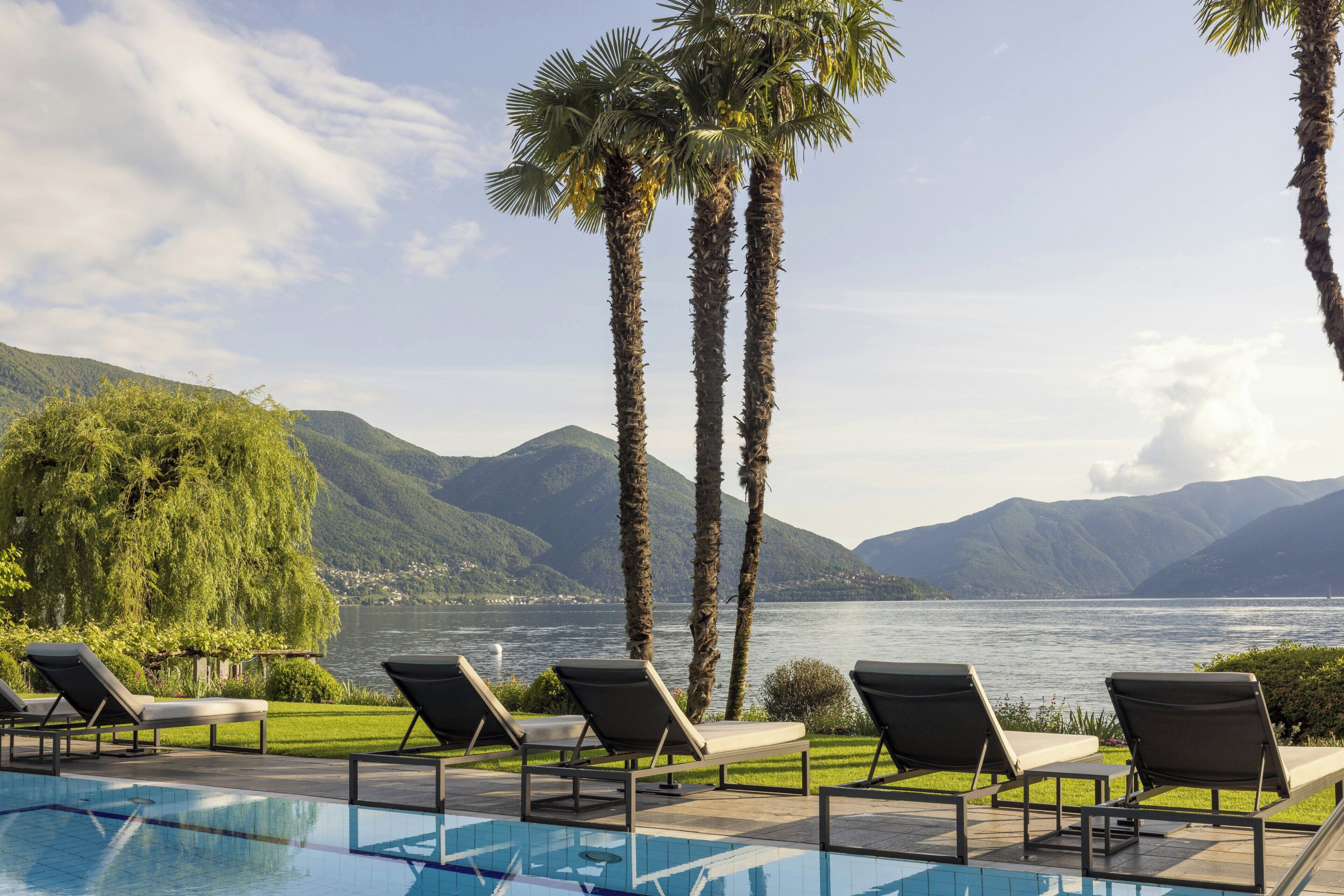 Un espace aménagé au bord de la piscine, avec des chaises longues et une vue sur un lac et des montagnes.