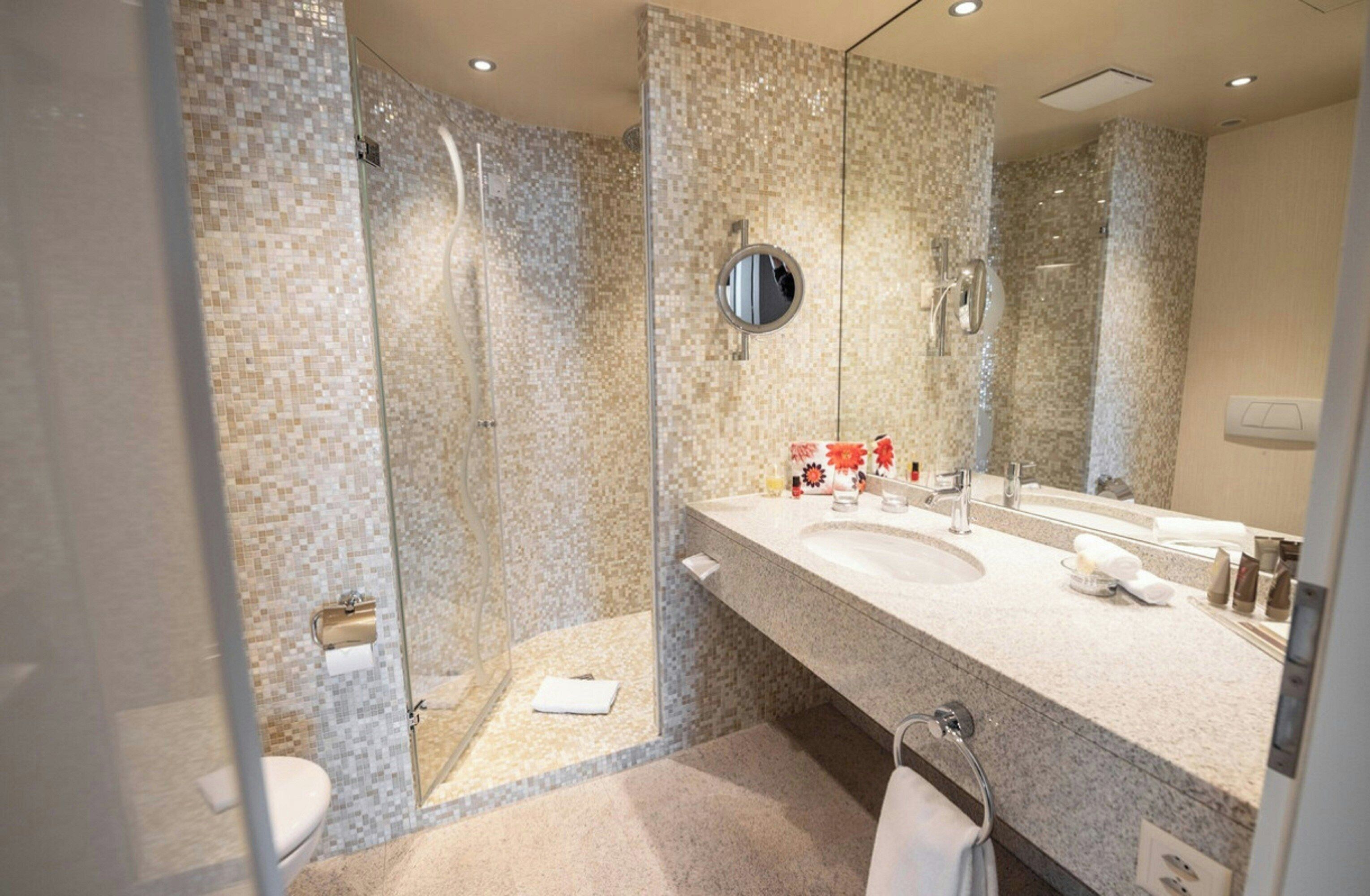 Un baño moderno con ducha acristalada, un espejo grande y encimera de granito.
