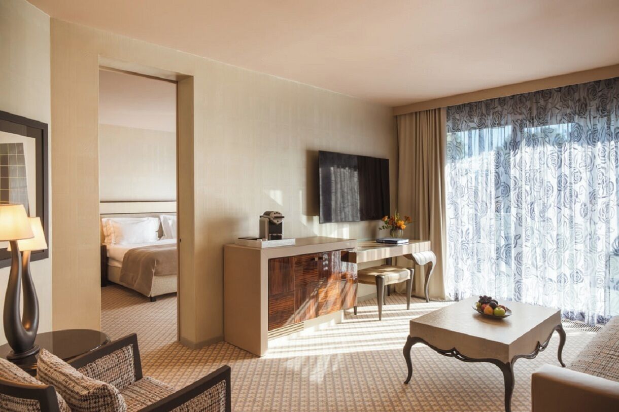 Quarto de hotel com cama, escrivaninha, cadeira, mesa e televisão.
