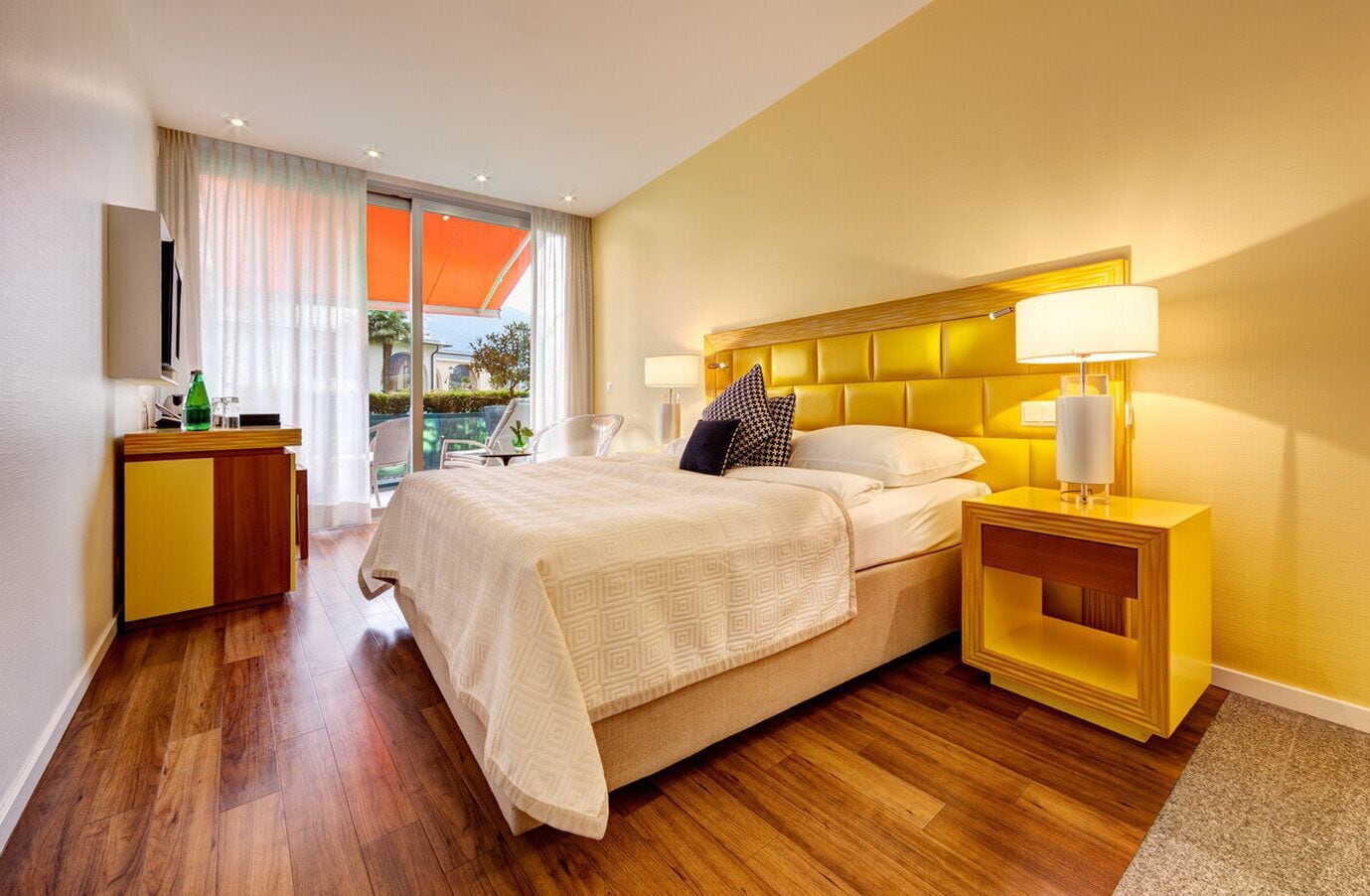 Habitación de hotel con cama, mesitas de noche, televisor y vistas al exterior.