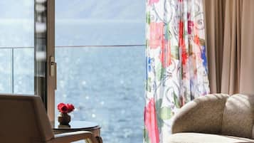 Een kamer met uitzicht op zee, een bloemen gordijn, een stoel en een kleine tafel met een bloevas.