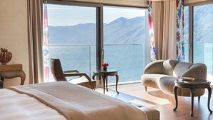 A hotel room with a large bed, a sofa, a small table, and a view of the sea and mountains. - Hotel Eden Roc (Ascona)