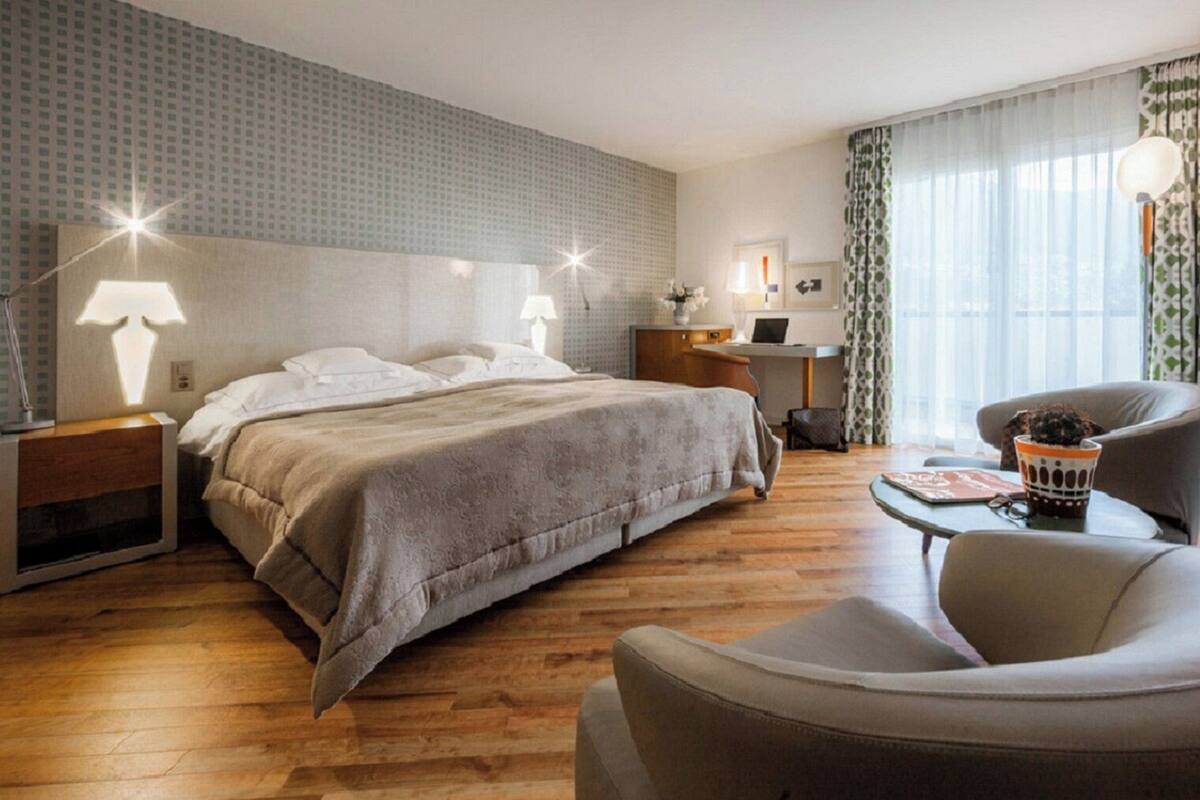 A hotel room with a large bed, a desk, a chair, and a lamp.