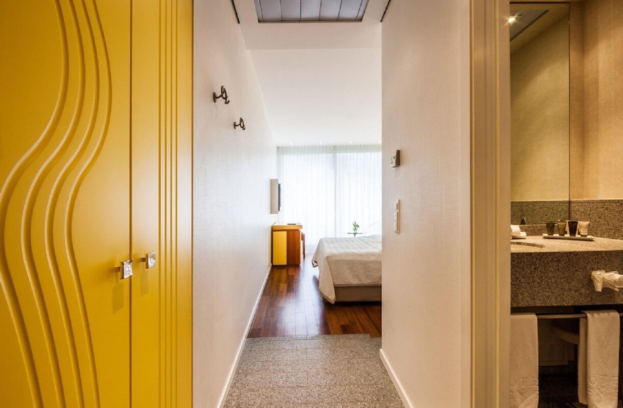 Ein Hotelzimmer mit Bett, Schreibtisch und einem Badezimmer mit Waschbecken und Spiegel.