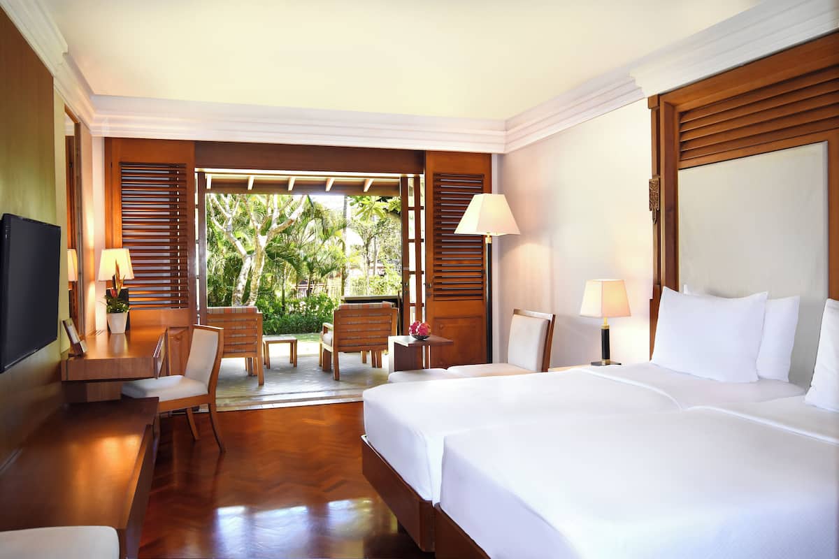A hotel room with a large bed, a desk with a chair, a TV, and a window with a view of greenery.