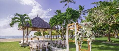 A beachside wedding setup with a gazebo, white chairs, and floral decorations.