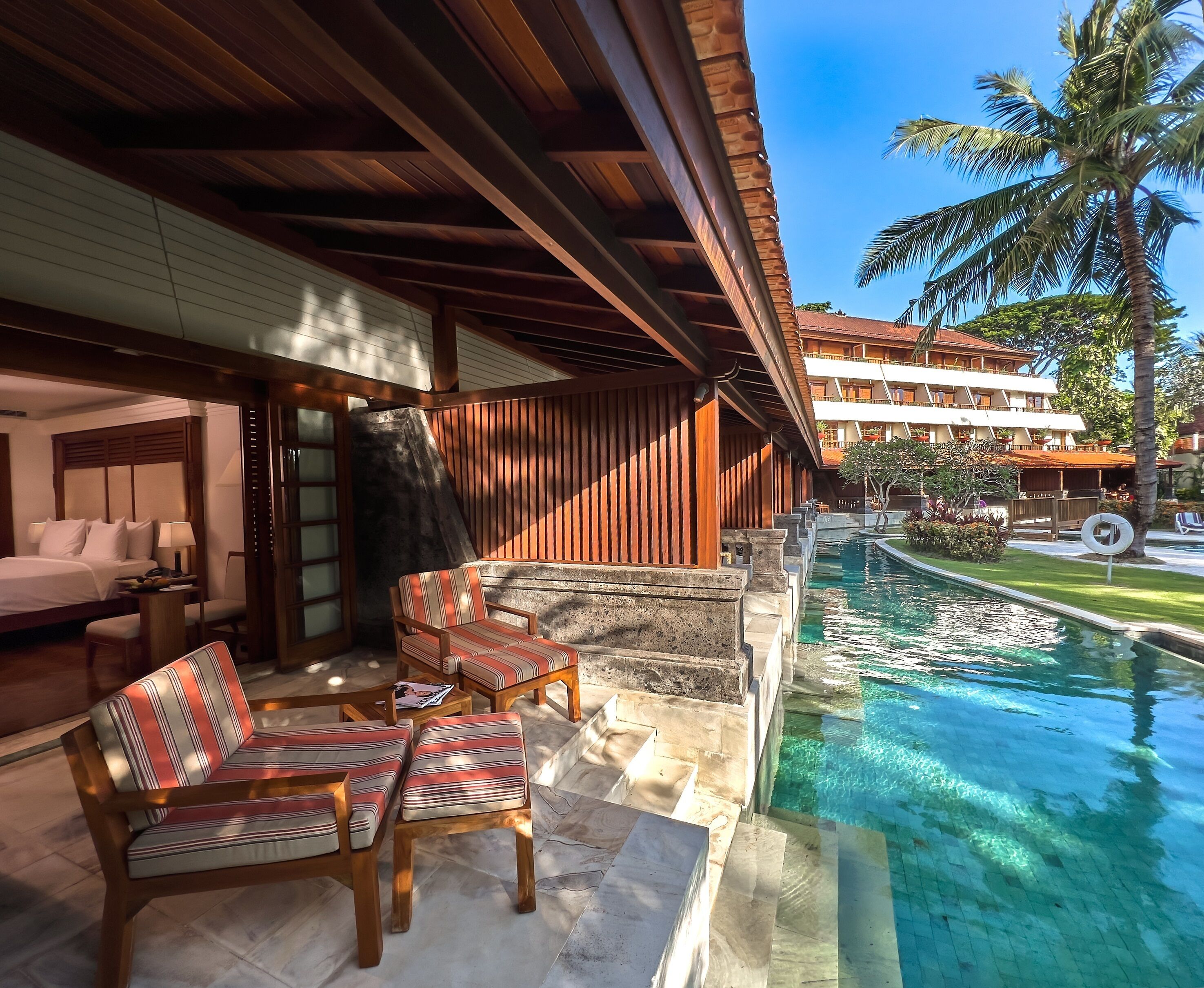 A poolside area with wooden furniture, a clear pool, and a view of a resort building.